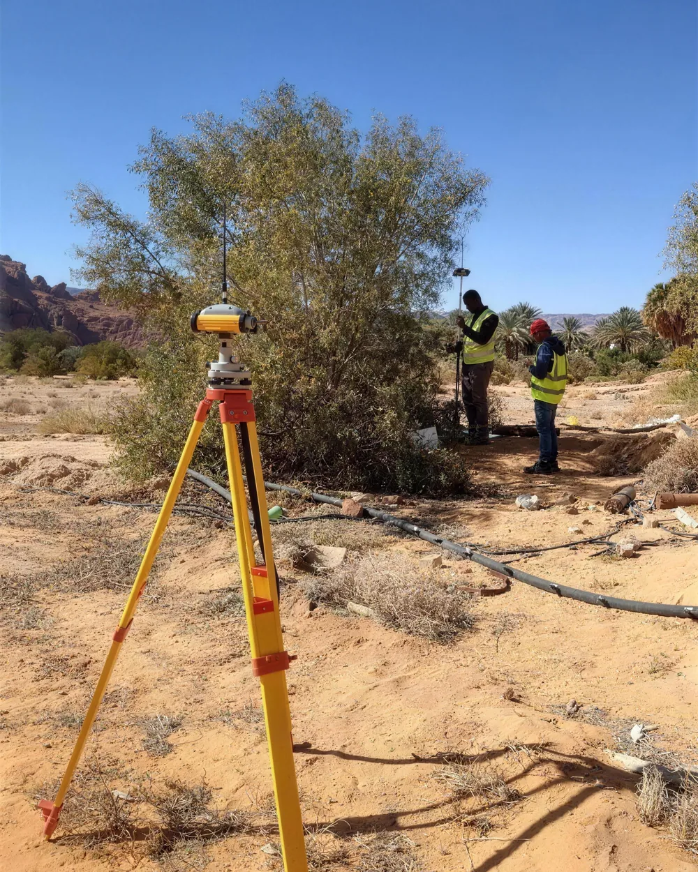 Total station set up beside acacia scrub, crew behind